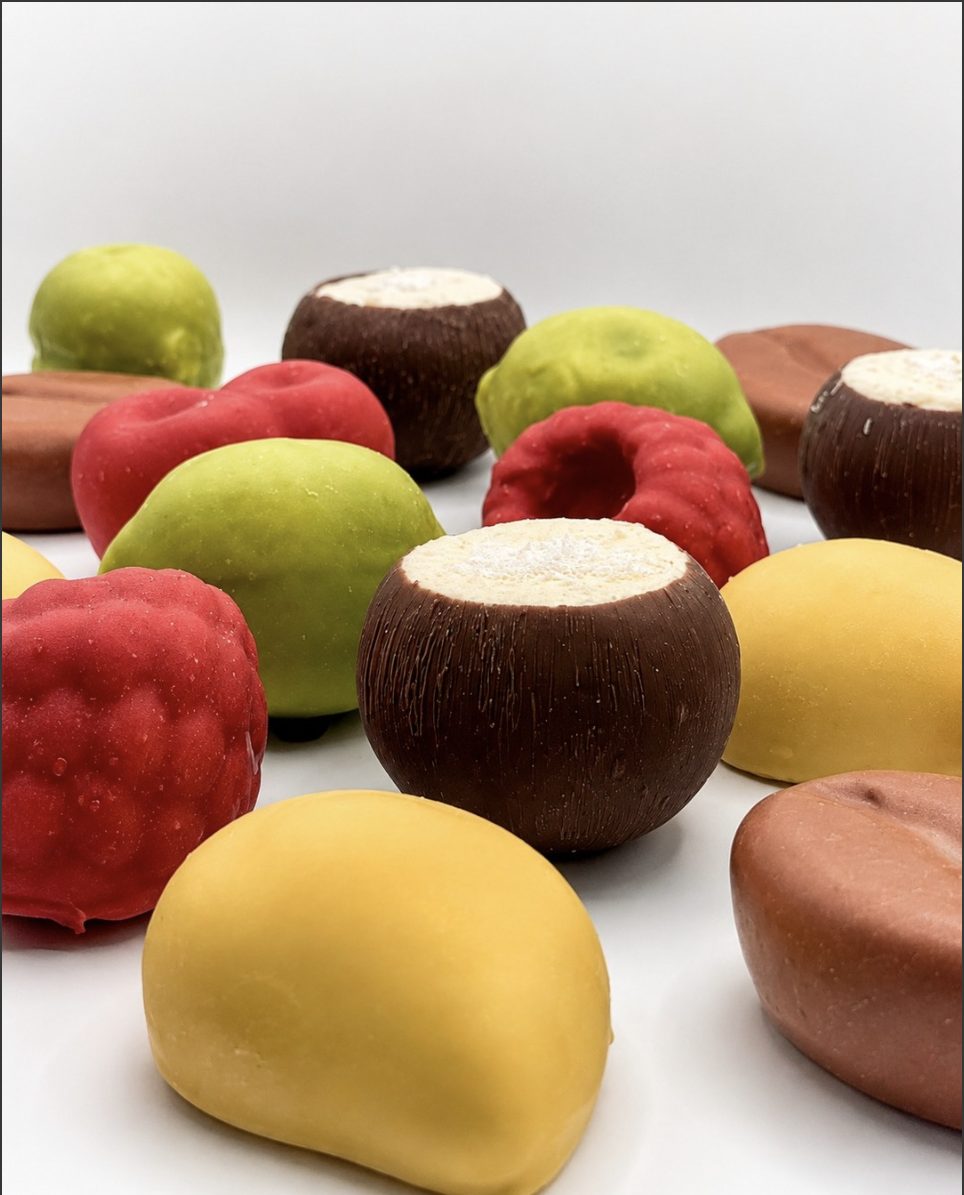 An assortment of glazed mousse cakes in raspberry red, lime green, mango yellow and chocolate.