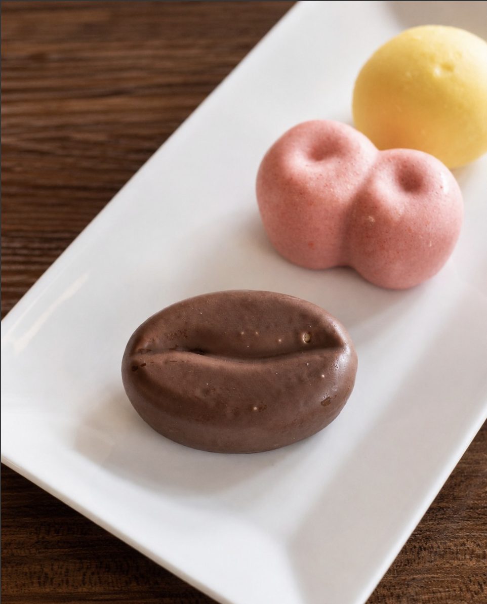 A chocolate coffee-bean shaped mousse dessert on a white plate, photographed close up.